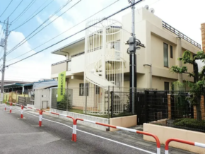 Two-story beige building with a white spiral exterior staircase, fenced yard, and orange-and-white traffic barriers along a residential street.