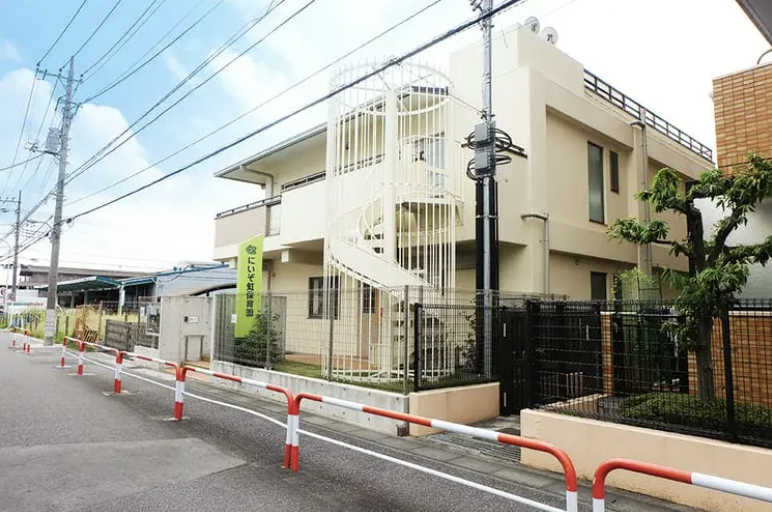 Two-story beige building with a white spiral exterior staircase, fenced yard, and orange-and-white traffic barriers along a residential street.