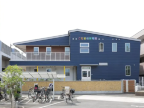 Blue two-story daycare center with a white entrance and a row of bicycles parked outside, a small fenced area in front.