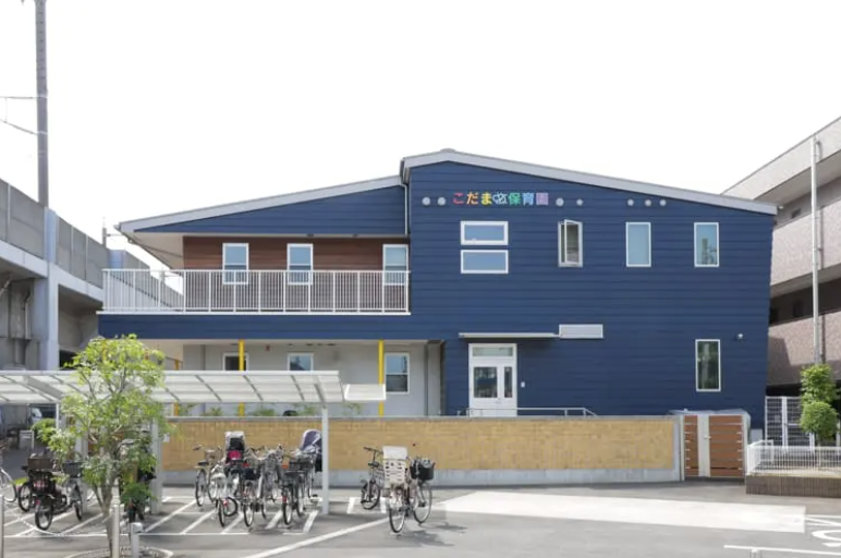 Blue two-story daycare center with a white entrance and a row of bicycles parked outside, a small fenced area in front.