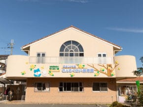 Front view of a beige daycare building with a large arched window, colorful cartoon characters, and a welcoming sign beneath a clear blue sky.