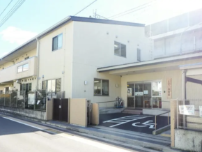 Exterior of a beige medical clinic with a marked disabled parking space near the entrance, along a street.