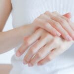 Person cradling their abdomen with both hands on a white ribbed shirt