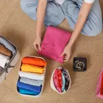 Top-down view of a person packing a suitcase with neatly folded clothes in colorful stacks on a woven rug